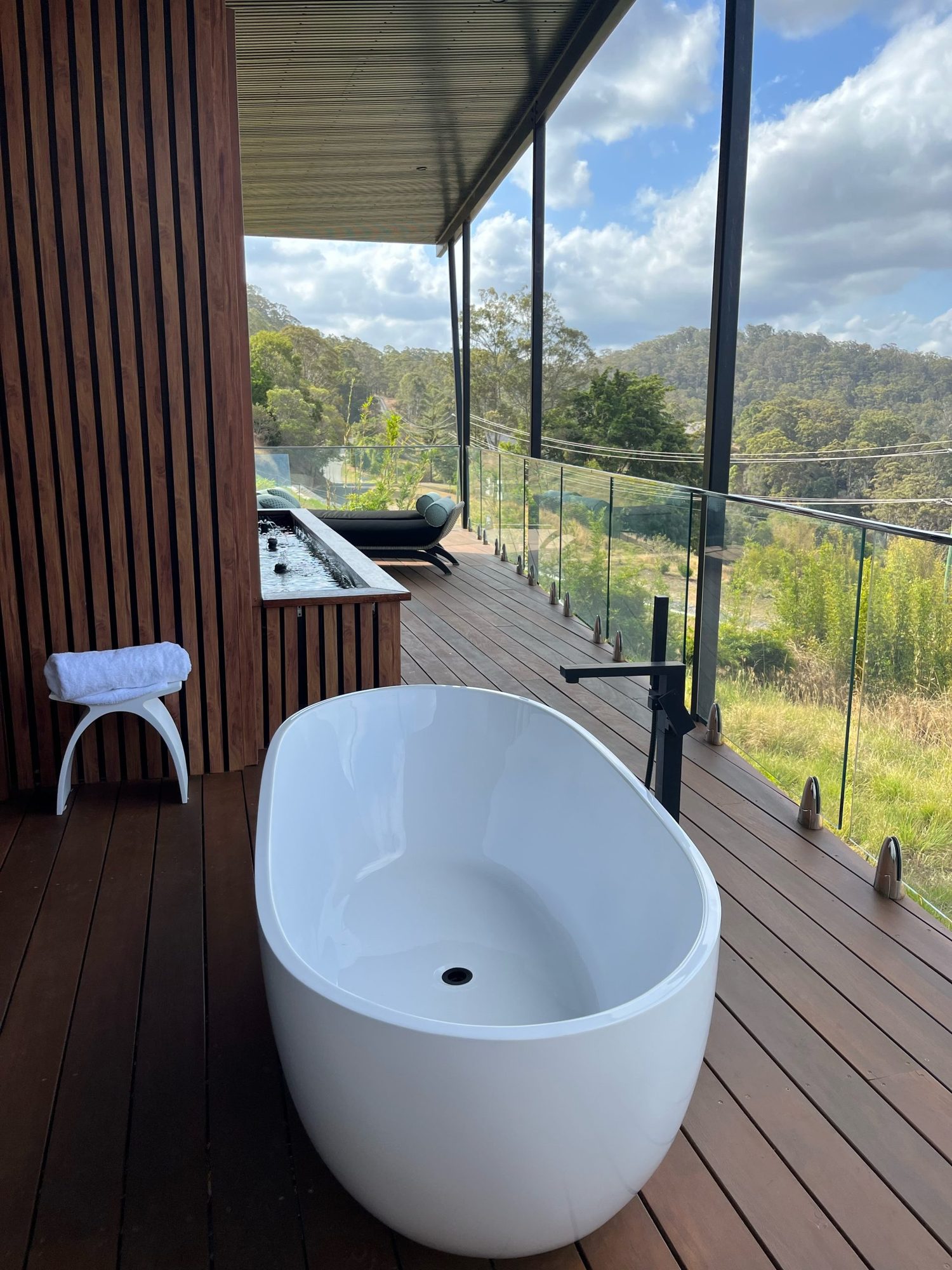 Freestanding white bathtub on a Spa Villa deck with the hinterland beyond the glass balustrade