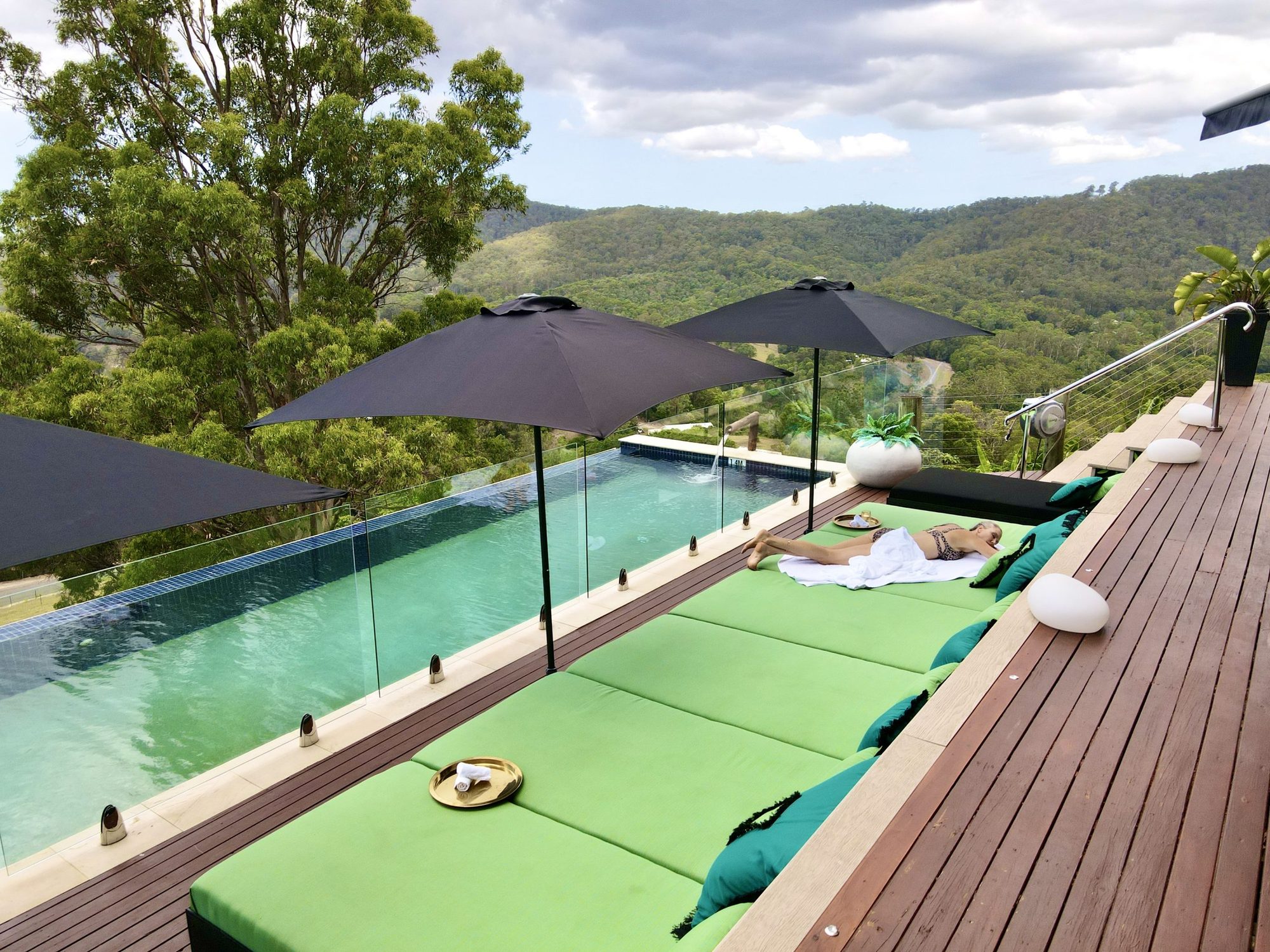 Long green loungers along the infinity pool under umbrellas