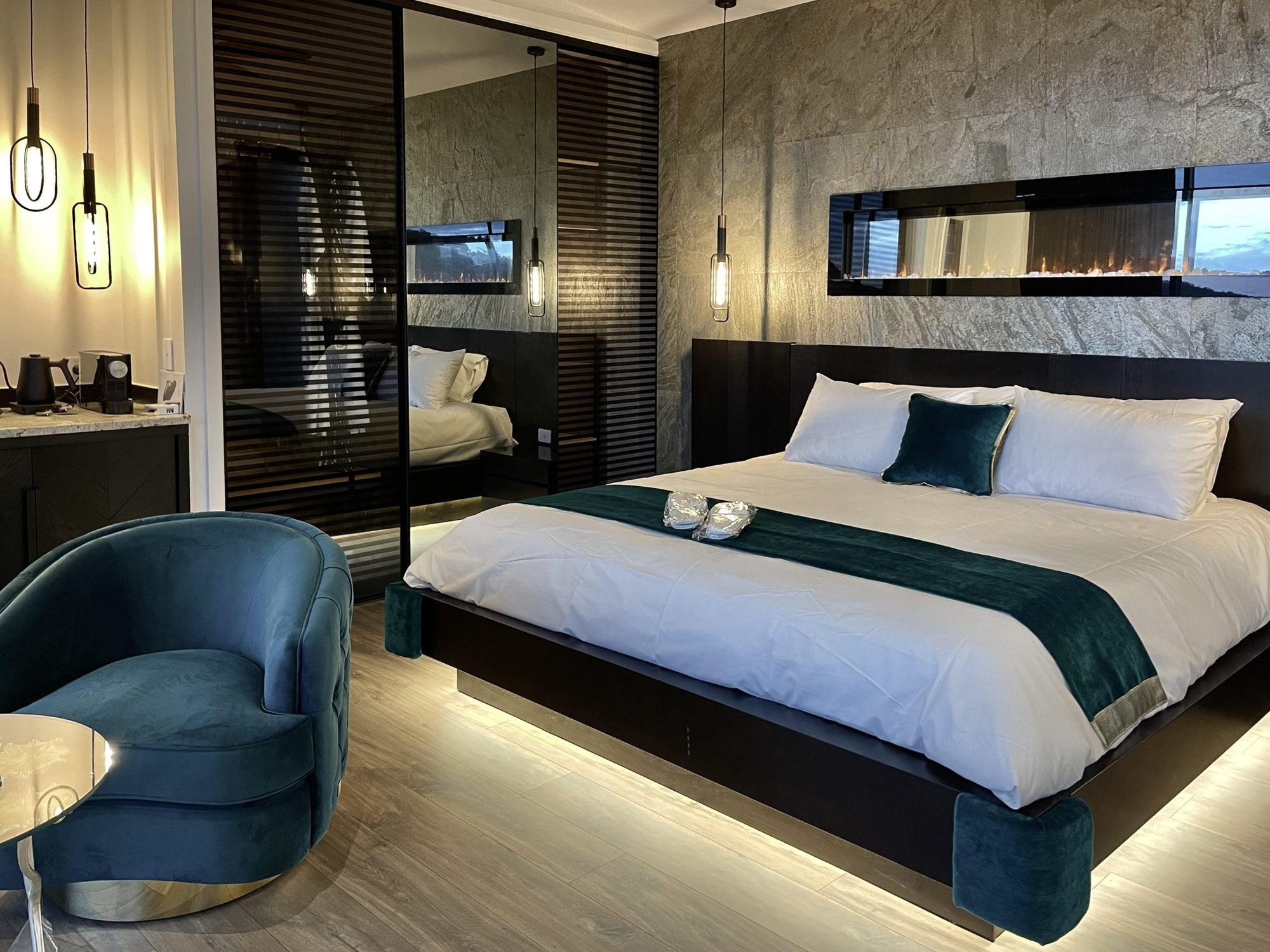 Spa Villa bedroom with king bed, teal velvet chair and linear fireplace