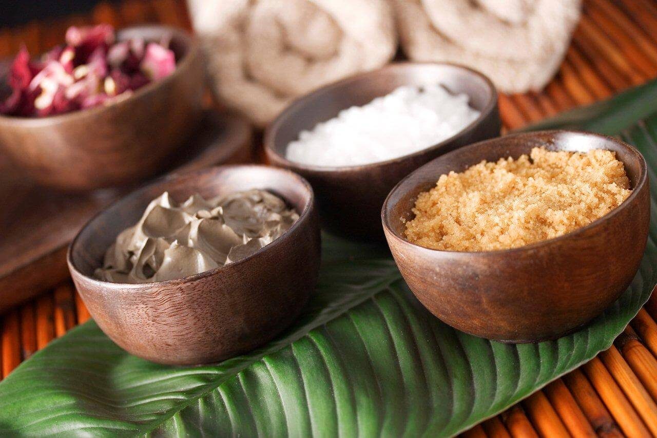 Wooden bowls of salt, sugar scrub and mud on a palm leaf